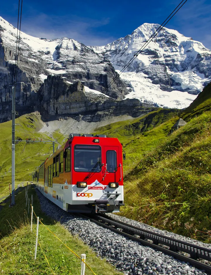 Red Jungfrau railway train climbing green meadows below the Eiger in Switzerland